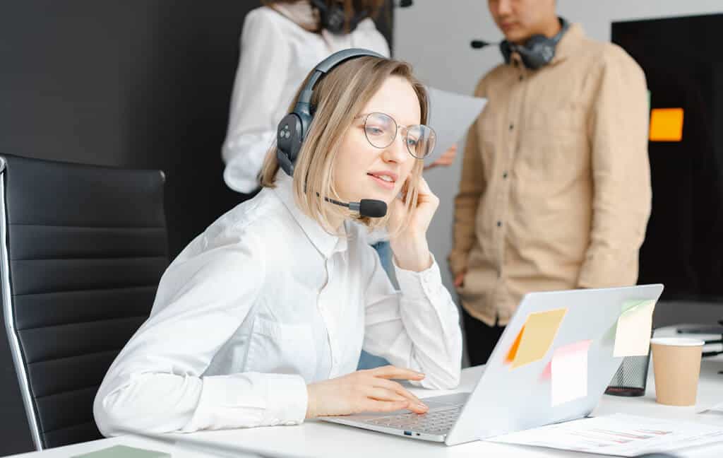 IT support professional working at a laptop while colleagues review a document